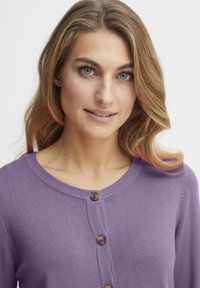Ljubičasti pleteni kardigan s okruglim izrezom, s gumbom za zatvaranje i rebrastom teksturom na patenti. Glatka, mekana tkanina.