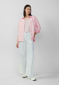Lichtroze oversized button-up shirt, witte V-hals t-shirt en wijde lichtblauwe broek. Witte sneakers maken de outfit compleet.