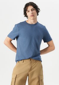 Blauw T-shirt met korte mouwen en ronde hals, gemaakt van een gestructureerde stof, gecombineerd met beige cargoshorts met zijzakken en een relaxte pasvorm.