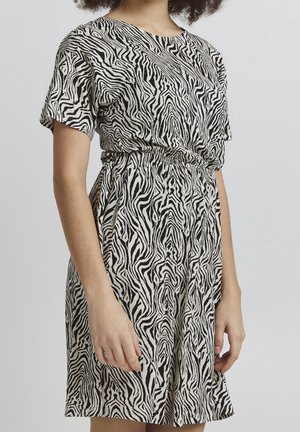 Vrouw draagt een jurk met korte mouwen tot op de knie met een zwart-witte zebraprint en een elastische tailleband.