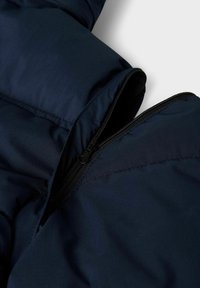Detalles de una chaqueta acolchada de color azul marino que presenta una apertura con cremallera, textura suave y tela lisa con sutilezas en los acabados de costura.