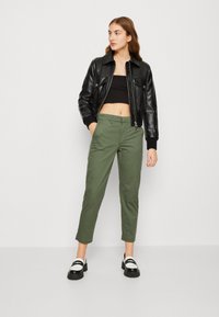 Black quilted leather jacket, cropped black top, olive green pants, and black shoes with white accents. Straight-leg design and clean lines.