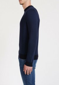 Pull-over en maille bleu marine avec un motif texturé, col rond, et poignets et ourlet côtelés. Associé à un jean en denim bleu clair.