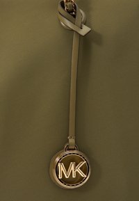 Borsa a tracolla verde oliva con texture liscia, caratterizzata da un emblema circolare in tono oro con logo "MK" e un accento in pelle annodata.