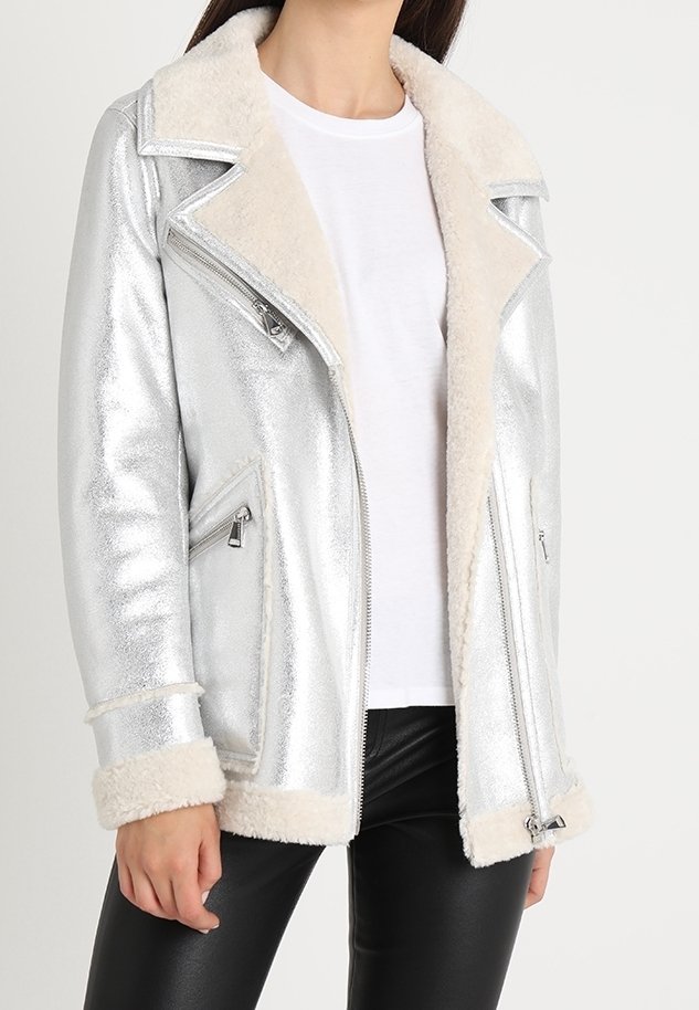 Giacca da motociclista in argento metallizzato con collare e polsini in pelliccia sintetica color crema, dotata di tasche con zip e design accorciato.