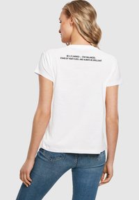 White cotton T-shirt with short sleeves featuring a text print on the back in black. Classic fit with a round neckline and soft texture.