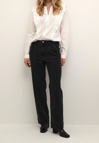 White button-up shirt with ruffled collar and lace trim, paired with high-waisted black denim pants with side pockets and wide legs.