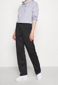 Šedá zkrácená mikina s kapucí, šňůrkami a logem, kombinovaná s černými rovnými kalhotami a bílými teniskami na neutrálním pozadí.