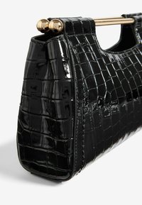 Bolso de mano de charol negro con textura de cocodrilo, forma estructurada y detalle de cierre en tono dorado en la parte superior.