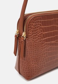 Brown crocodile-embossed leather bag with gold-tone hardware, dual zippers, and slim shoulder strap. Compact rectangular shape.
