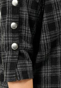 Czarna i szara koszula flanelowa w kratę z srebnymi zatrzaskami i textured tkaniną. Rękaw ma niewielkie rozcięcie przy mankiecie.