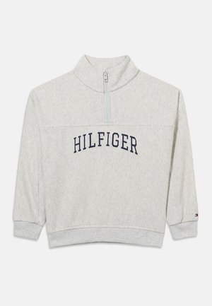 Hanorac gri deschis cu fermoar scurt, cu mansete și tiv striate, inscripția „HILFIGER” pe piept și mic logo pe mânecă stângă.
