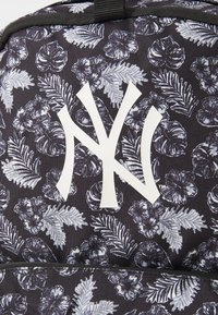 Black backpack with a floral pattern featuring white ferns and flowers, prominently displaying a white New York Yankees logo.