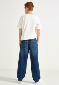Vit kortärmad t-shirt i kombination med lösa blå denimjeans. Jeansen har två bakfickor och en rak benform.