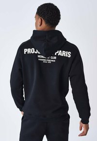 Sudadera negra hecha de tejido suave, con un gran logo blanco impreso en la parte posterior. Mangas largas, capucha y detalle de ribete en el dobladillo.