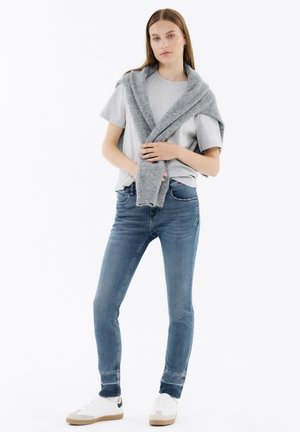 Gray t-shirt layered with a gray knitted sweater, paired with blue skinny jeans and white sneakers. Smooth fabric and fitted design.