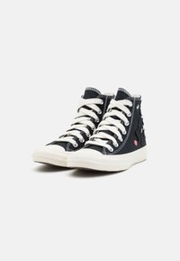 Czarne sneakersy typu high-top z białymi sznurówkami i podeszwami, z subtelnymi haftowanymi wzorami kwiatowymi po zewnętrznych stronach, wyeksponowane na białym tle.