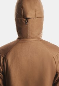 O persoană îmbrăcată într-o jachetă căptușită maro, cu glugă, văzută din spate pe un fundal simplu deschis.