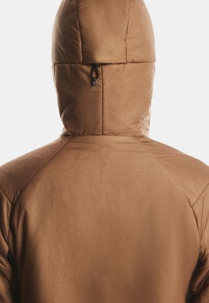 Persona con una chaqueta acolchada marrón con capucha, vista desde atrás sobre un fondo claro y liso.