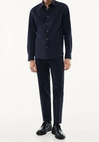 Chemise à manches longues bleu marine avec fermeture à boutons, coupe ajustée ; associée à un pantalon foncé assorti et des chaussures noires à lacets. Tissu lisse, design minimaliste.