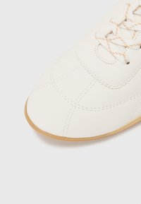 Baskets en cuir blanc avec un bout arrondi, dotées d'une semelle en caoutchouc beige clair, d'un design à lacets et d'accents cousus sur le dessus.