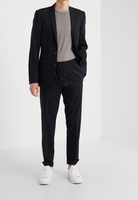 Czarny dopasowany blezer z dwoma guzikami, zestawiony z szarym t-shirtem z okrągłym dekoltem oraz czarnymi spodniami za kostkę z elastycznego materiału. Całość dopełniają białe sneakersy.