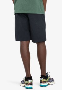 Dunkelblaue Shorts mit geradem Schnitt, kombiniert mit mehrfarbigen Sneakern, die ein strukturiertes Design und lebhafte Akzente aufweisen.