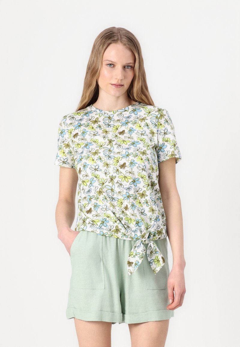 Blomstret kortermet topp med rund halslinning, med hvit bakgrunn og blå, grønn og brun mønstre. Kombinert med lyse grønne shorts.