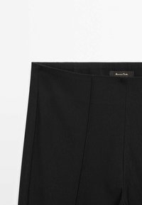 Pantalon noir taille haute avec coutures verticales et étiquette de marque visible à l'intérieur de la ceinture sur fond blanc.