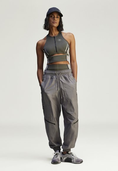 Sportoutfit met een donkergrijze cropped tanktop met een ritssluiting aan de voorkant, gecombineerd met lichtgrijze cargobroeken. Inclusief zakken en elastische manchetten.