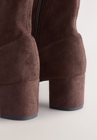 Hnedé semišové členkové čižmy s okrúhlou špičkou a blokovým podpätkom, s bočným zipsom a hladkou textúrou, zdôrazňujúce detaily švov.