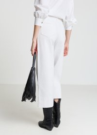 Weiße Hosen mit weitem Bein und Gesäßtaschen, kombiniert mit einer schwarzen Handtasche mit Fransen und kniehohen schwarzen Stiefeln mit strukturiertem Muster.