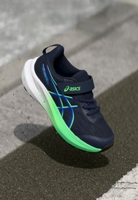 Baskets de sport bleu marine avec une tige texturée, des accents verts et bleus, et une semelle blanche. Dotées d'une bande Velcro pour un maintien sécurisé.