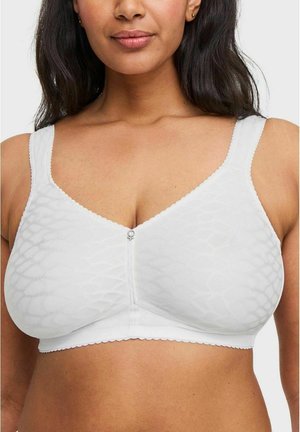 Vrouw die een witte draadloze beha met textuur draagt, met brede bandjes en een klein metalen hangertje aan de voorkant in het midden.