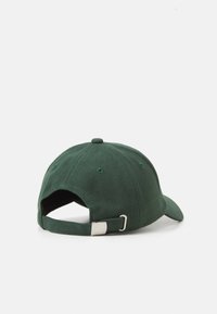 Green cotton cap with a curved brim, adjustable strap, and metal buckle. Features ventilation holes and a rounded top.