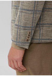 Brauner und beiger karierter Blazer aus einem strukturierten Stoff; verfügt über blaue Linien und vier braune Knöpfe an den Ärmelbündchen. Weicher Strickkragen.