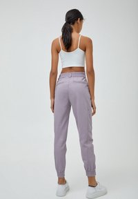 Pantalons cargo lilas avec une taille élastique, des poches latérales et des poignets fuselés, associés à un crop top blanc. Texture de tissu lisse.