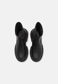Black leather ankle boots with elastic side panels, rubber soles, and textured detailing on the sole for grip, viewed from above.