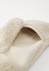 Tan, plush slipper with a textured, fluffy exterior and a soft fleece interior. Features a rounded shape and no visible hardware.