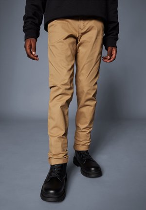 Beige chinos med slim fit og lige ben, parret med sorte snørebåndsstøvler med en kraftig sål. Glat stoftekstur.