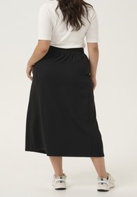 Zwarte, enkellange rok met een elastische tailleband, een gladde textuur en zonder zichtbare patronen. Gecombineerd met witte sneakers.