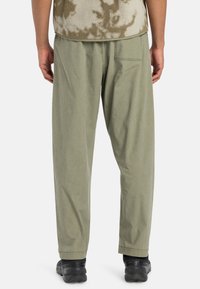 Khaki cotton pants with a relaxed fit, featuring side pockets and back patch pocket. Paired with a textured fleece top. Black shoes visible.