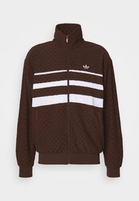 Ruskea vetoketjullinen takki, jossa on korkea kaulus, tekstuuripintainen kuvio ja kolme vaakasuoraa valkoista raitaa. Takissa on etutasku ja ribbireunat.