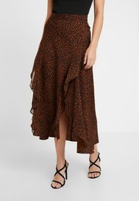 Jupe maxi en imprimé léopard marron en tissu léger, avec un ourlet ondulé et une fente haute sur la cuisse, assortie à des talons noirs à lanières.