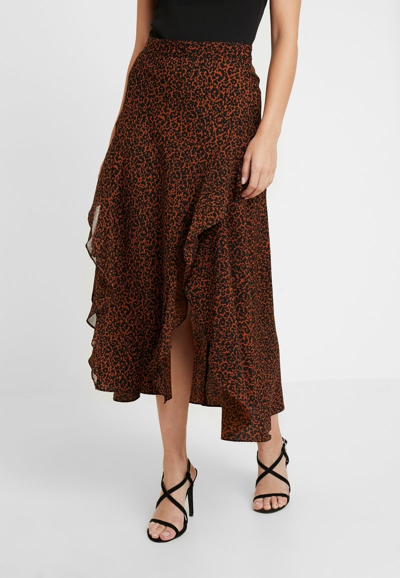Jupe maxi en imprimé léopard marron en tissu léger, avec un ourlet ondulé et une fente haute sur la cuisse, assortie à des talons noirs à lanières.