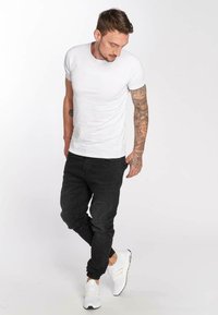 Camiseta blanca de manga corta, pantalones jogger negros y zapatillas blancas. Incluye tatuajes en el brazo. Conjunto simple y casual.