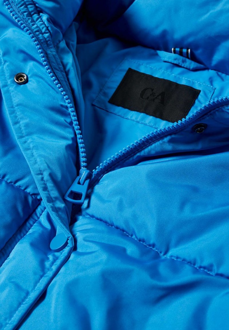 Interior de chaqueta acolchada azul brillante, con un zipper que tiene un tirador azul y una etiqueta de tela negra con el logo "C&A" cosido.