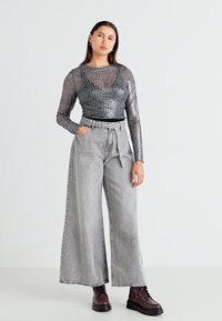 Blusa transparente de mangas longas com estampa animal em cinza, combinada com calças largas de cintura alta em cinza e botas robustas castanhas com atacadores.