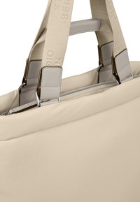 Beige tygväska med dubbla platta handtag, silverfärgade detaljer och dragkedjestängning. Slät yta med logotypdetalj på remmen.