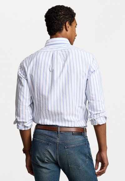 White shirt with light blue vertical stripes, button-down collar, rolled sleeves, paired with dark blue jeans and a brown belt.